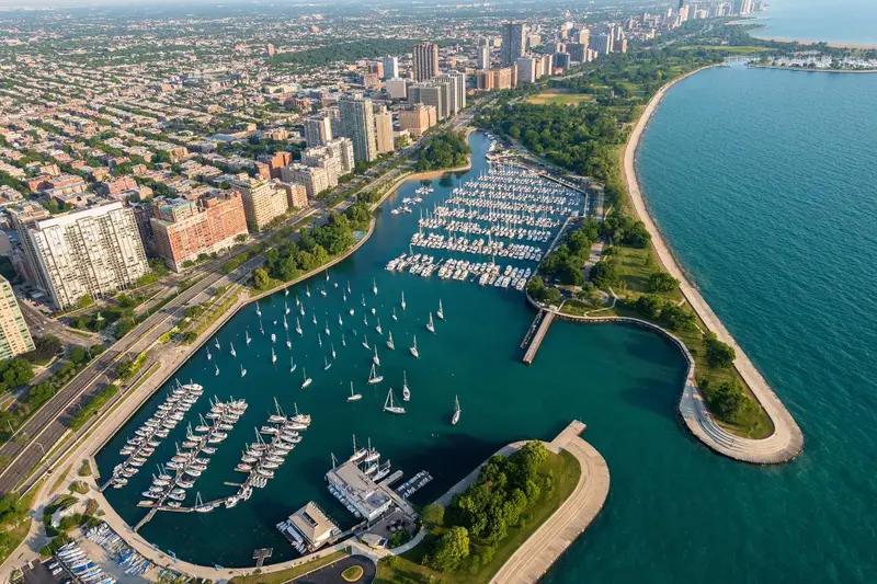 Aerial view of Belmont Harbor in Chicago's Lakeview neighborhood, showing hundreds of docked boats on Lake Michigan surrounded by green parks, Lake Shore Drive, and dense high-rise apartment buildings.