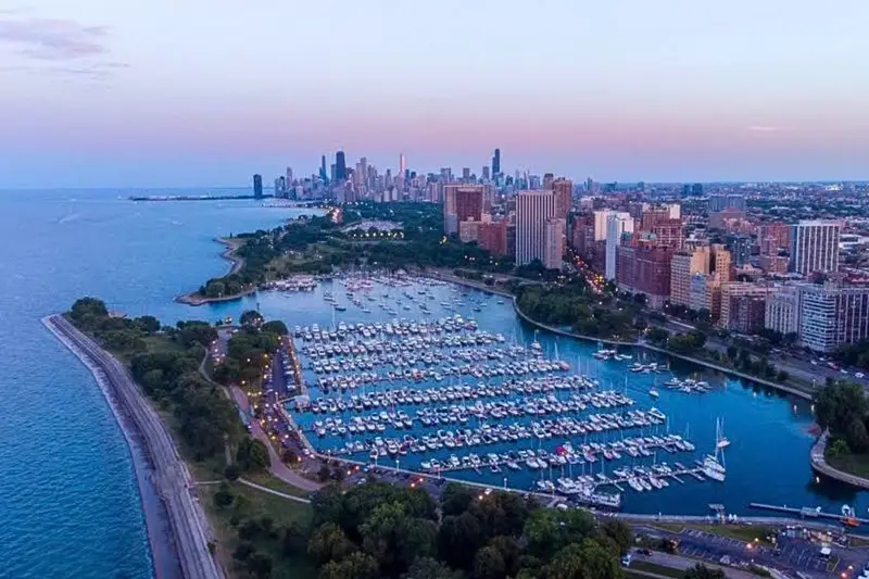 Aerial view of Belmont Harbor in Chicago's Lakeview 60657 neighborhood with boats docked and the downtown skyline in the background.