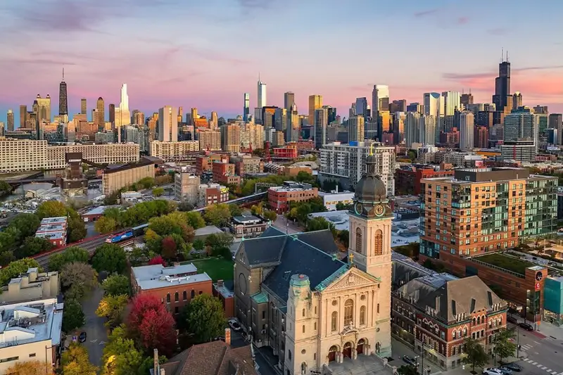 Breathtaking aerial sunset view of West Town Chicago featuring historic neighborhood churches and the glowing downtown city skyline.