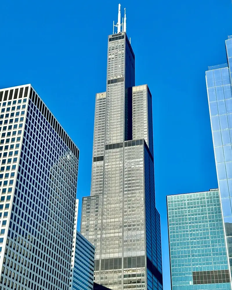 Looking up at the iconic black Willis Tower against a bright blue sky in downtown Chicago.
