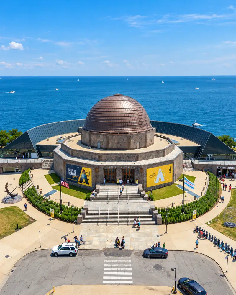Aerial view of the front entrance and bronze dome of the Adler Planetarium in Chicago, with the vast blue waters of Lake Michigan directly behind it.