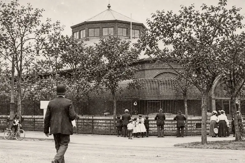 Archival sepia photograph of visitors in early 20th-century attire observing outdoor animal cages at Chicago's Lincoln Park Zoo.