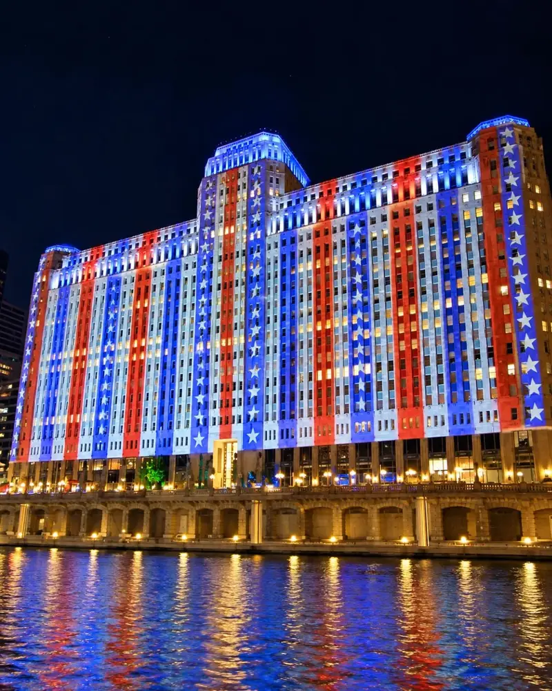 The massive facade of the Merchandise Mart building in Chicago illuminated at night with a vibrant red, white, and blue digital art projection.