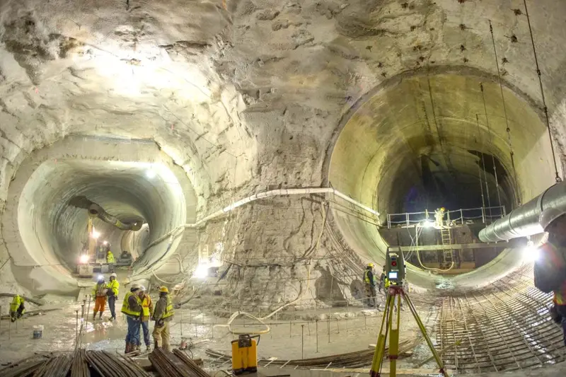 Construction workers and surveying equipment inside a massive, cavernous underground rock tunnel, showing the jaw-dropping scale of Chicago's Deep Tunnel stormwater system.