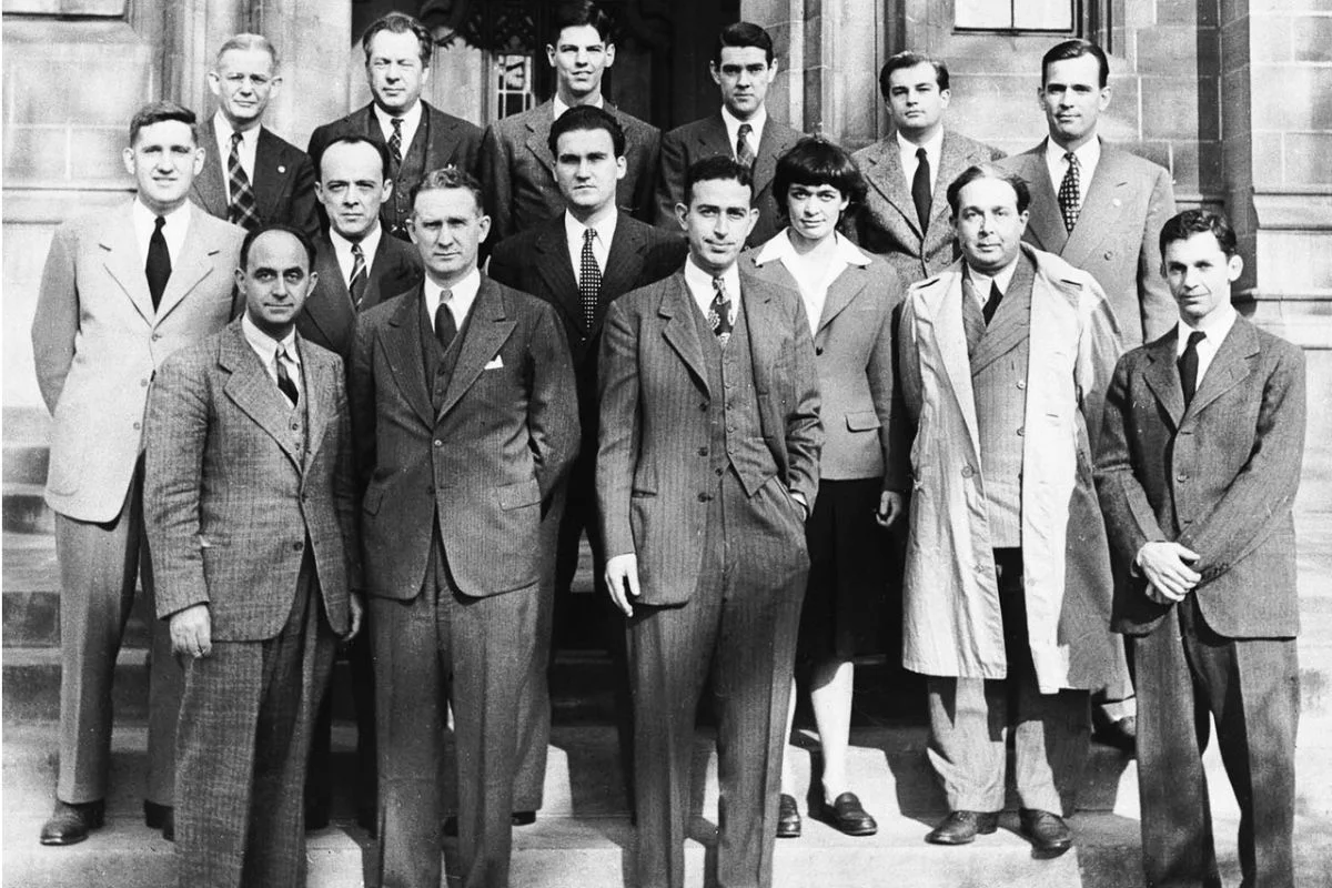 Black and white archival photograph of the Chicago Pile-1 scientific team posing together on the stone steps of a University of Chicago building, featuring project leader Enrico Fermi and Leona Woods, the only woman on the team.