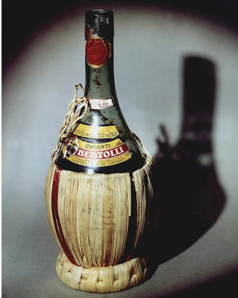 Color photograph of the historic straw-wrapped Bertolli Chianti bottle, featuring faded handwritten signatures across its woven base, which was shared by scientists to celebrate the successful Chicago Pile-1 nuclear reactor experiment in 1942.