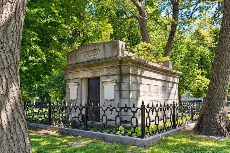 A large 19th-century stone mausoleum with the name COUCH carved at the top, surrounded by a black decorative iron fence and large green trees in Chicago's Lincoln Park.