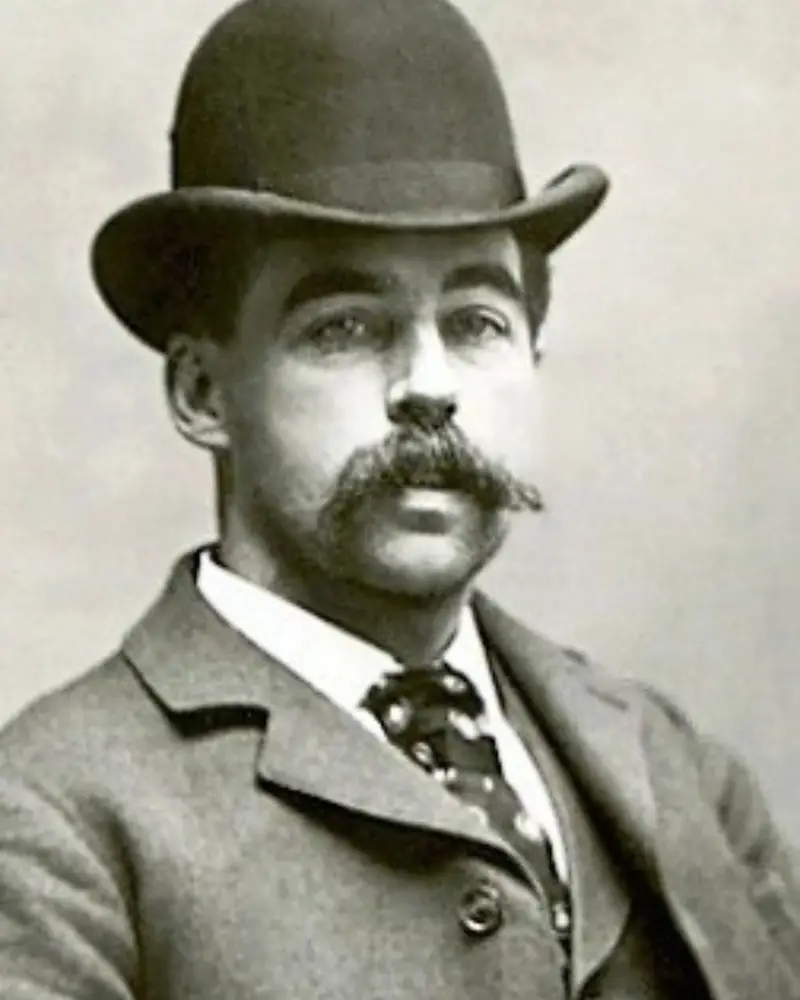 Historical sepia portrait of H.H. Holmes wearing a black bowler hat, tweed suit jacket, and displaying a mustache.