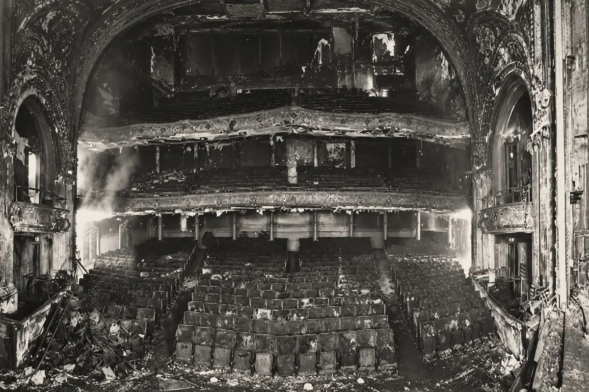 Panoramic black-and-white archival photograph showing the interior auditorium of the Iroquois Theatre after the 1903 fire, revealing structurally intact seating covered in debris and soot.