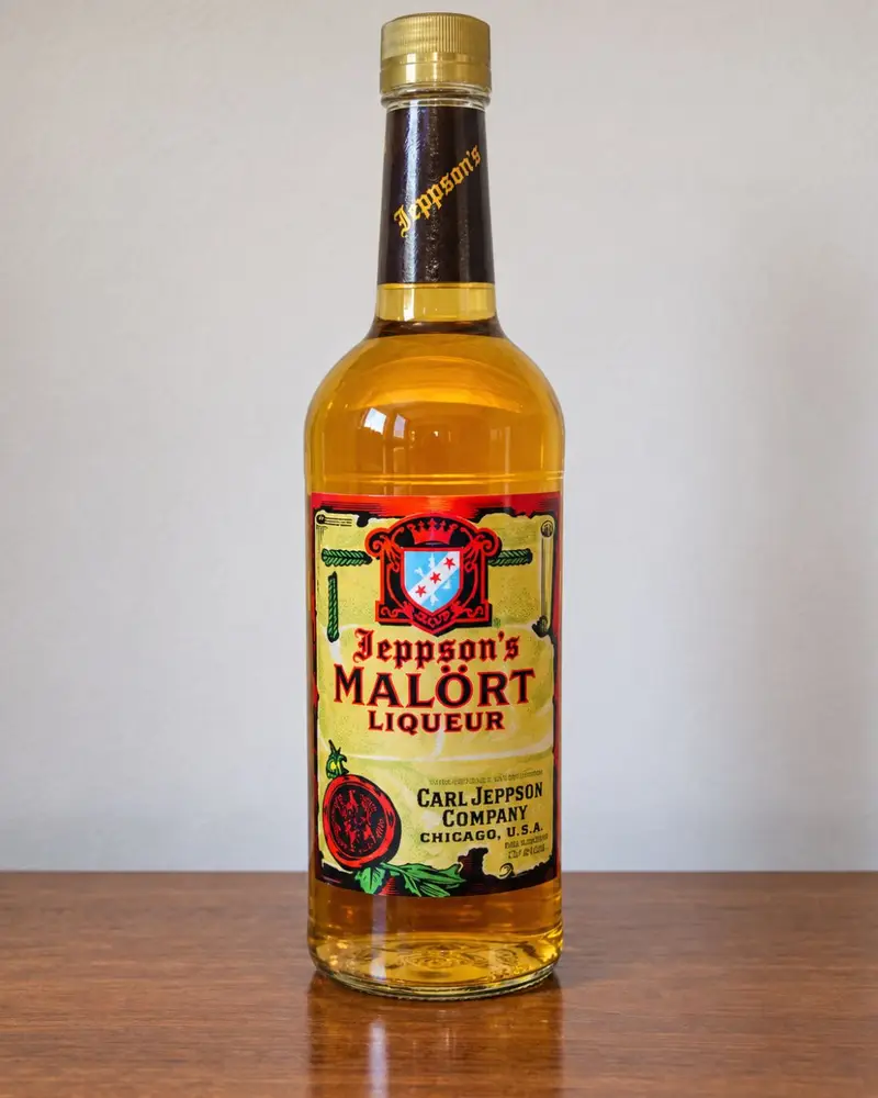 A full bottle of Jeppson's Malört liqueur sitting on a wooden table against a plain white background.