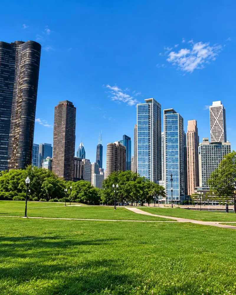 A peaceful view of the Chicago skyline from the green lawns of Milton Lee Olive Park on a clear sunny day, featuring Lake Point Tower and the Streeterville high-rises.