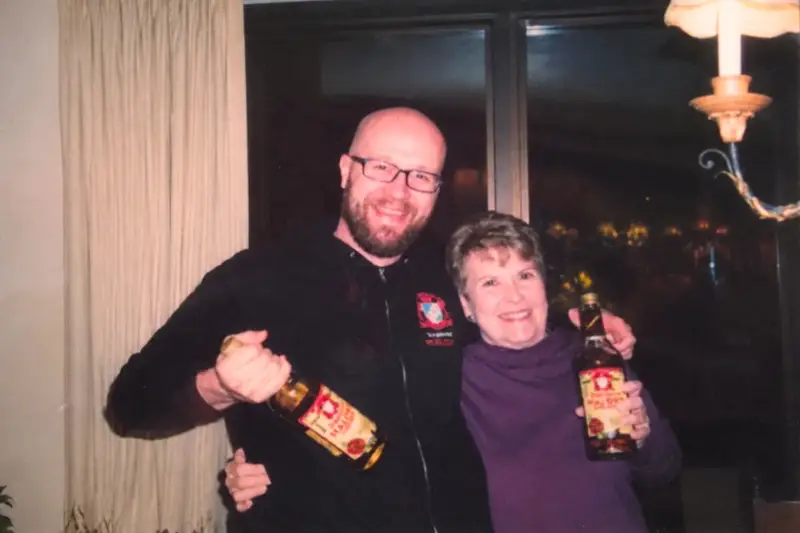A candid, vintage-style photograph of former Jeppson's Malört owner Patricia Gabelick and brand ambassador Sam Mechling smiling together while holding bottles of Malört.