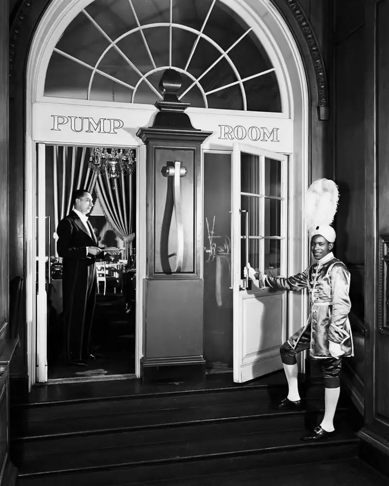 A vintage photograph of The Pump Room entrance at the Ambassador East Hotel in Chicago, featuring a waiter in a feathered turban.