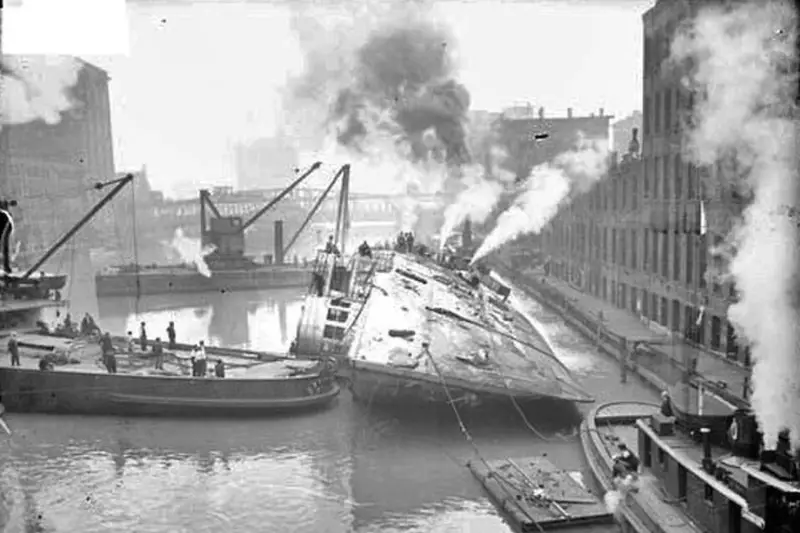 Archival photograph dated August 14, 1915, showing the capsized hull of the SS Eastland surrounded by smoking tugboats and heavy salvage cranes in the Chicago River.