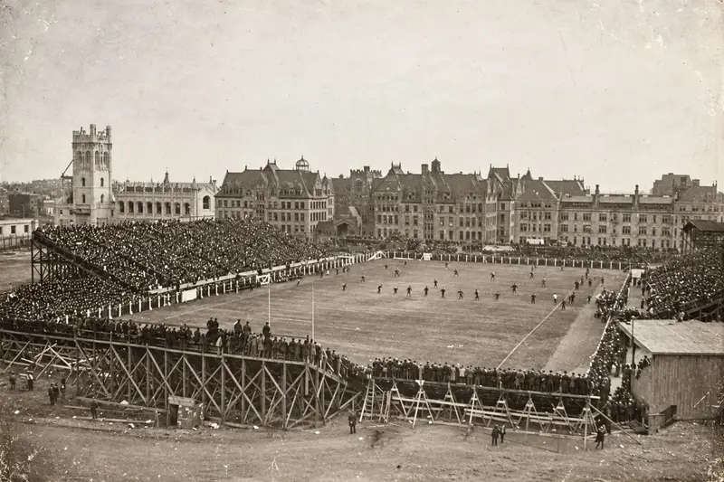 Archival photograph of a crowded football game at the University of Chicago's Alonzo Stagg Field in the early 1900s, featuring the massive wooden viewing stands where the Manhattan Project later built the world's first nuclear reactor.