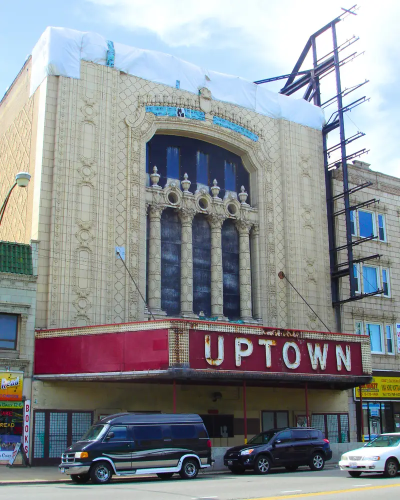 The exterior facade and iconic marquee of the historic Uptown Theatre on North Broadway in Chicago, featuring ornate terra cotta details and boarded windows.