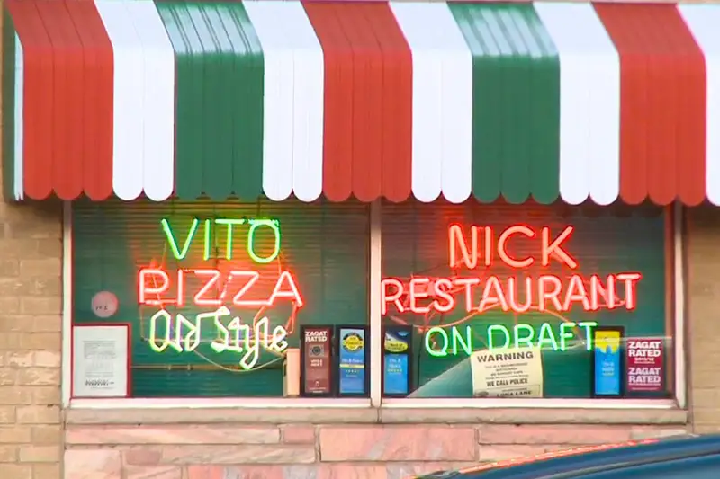 Vintage neon signs reading 'Vito Pizza Old Style' and 'Nick Restaurant On Draft' glowing in the window of Vito & Nick's Pizzeria in Chicago, sitting beneath a green, white, and red striped awning.