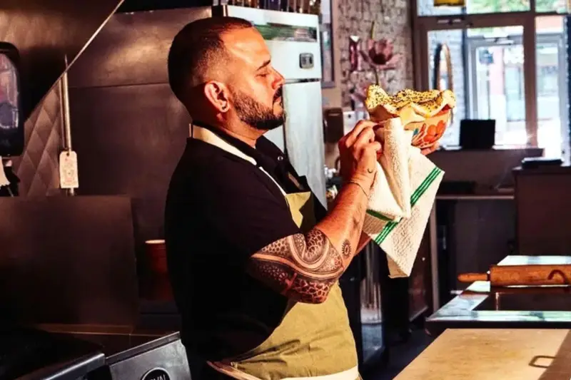 Chef Zubair Mohajir standing in the Mirra Chicago kitchen holding the restaurant's signature lamb barbacoa dum biryani, baked under a flaky roti crust.